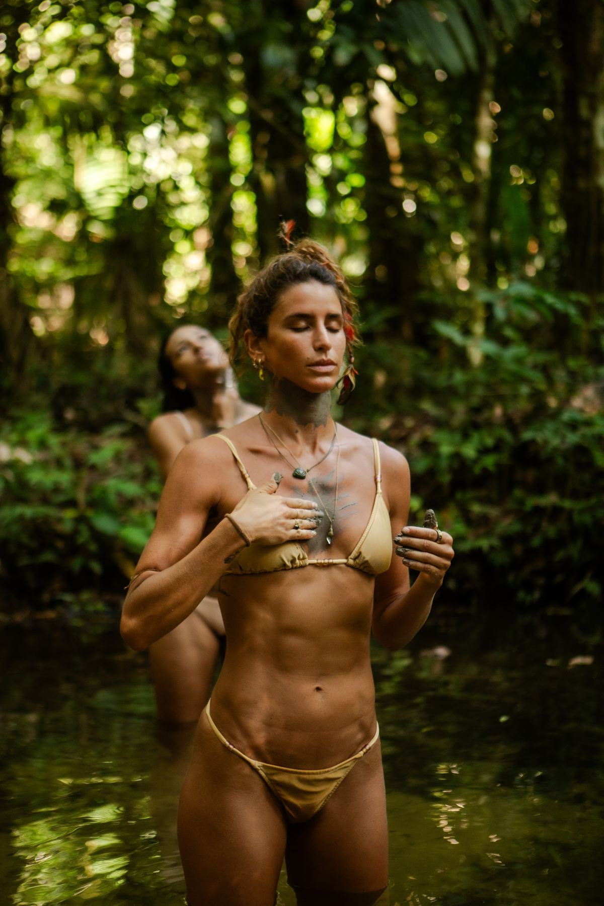 Mulher dentro da água de um igarapé cercado pela floresta