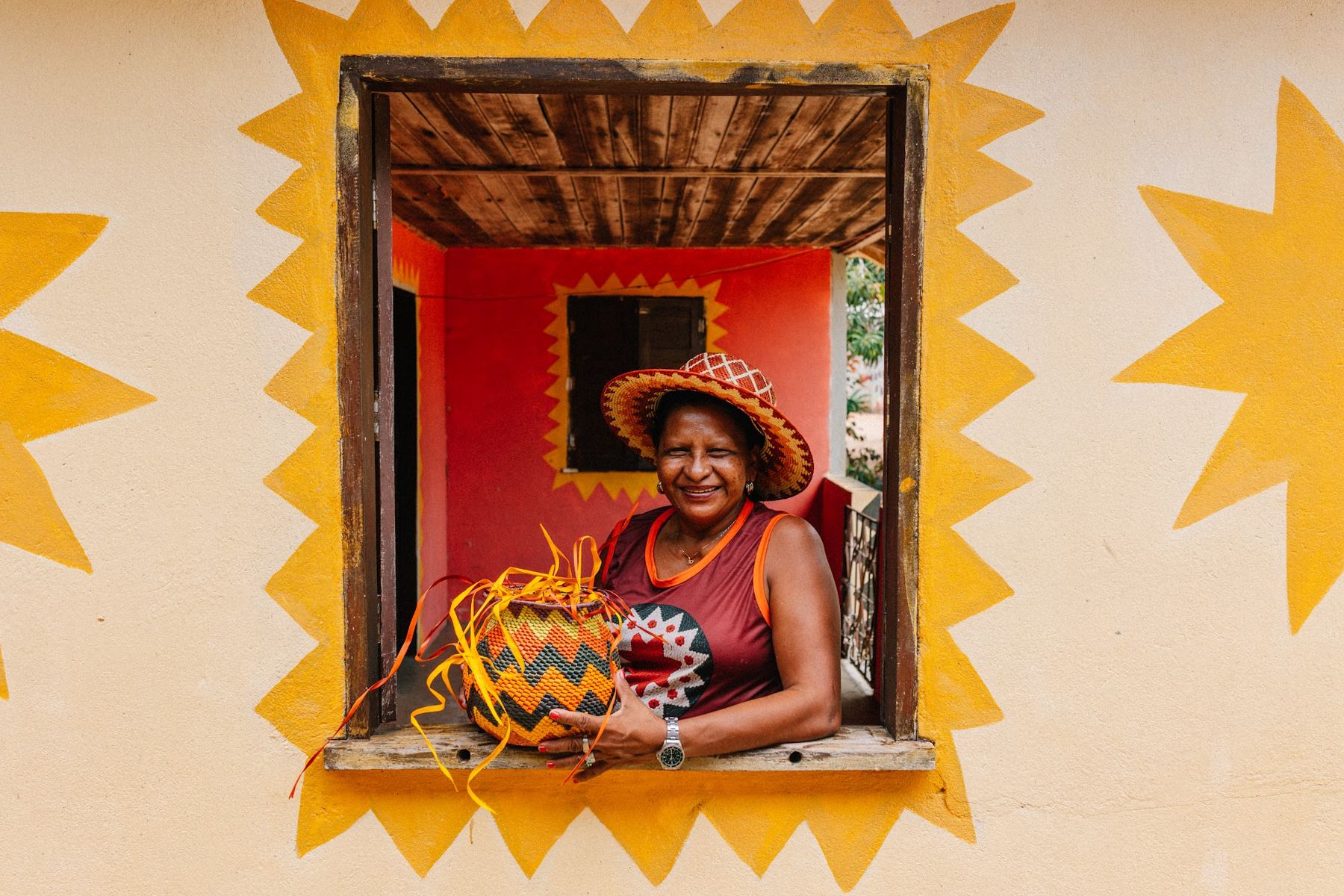 Mulher sorrindo numa janela pintada, segurando uma peça de artesanato
