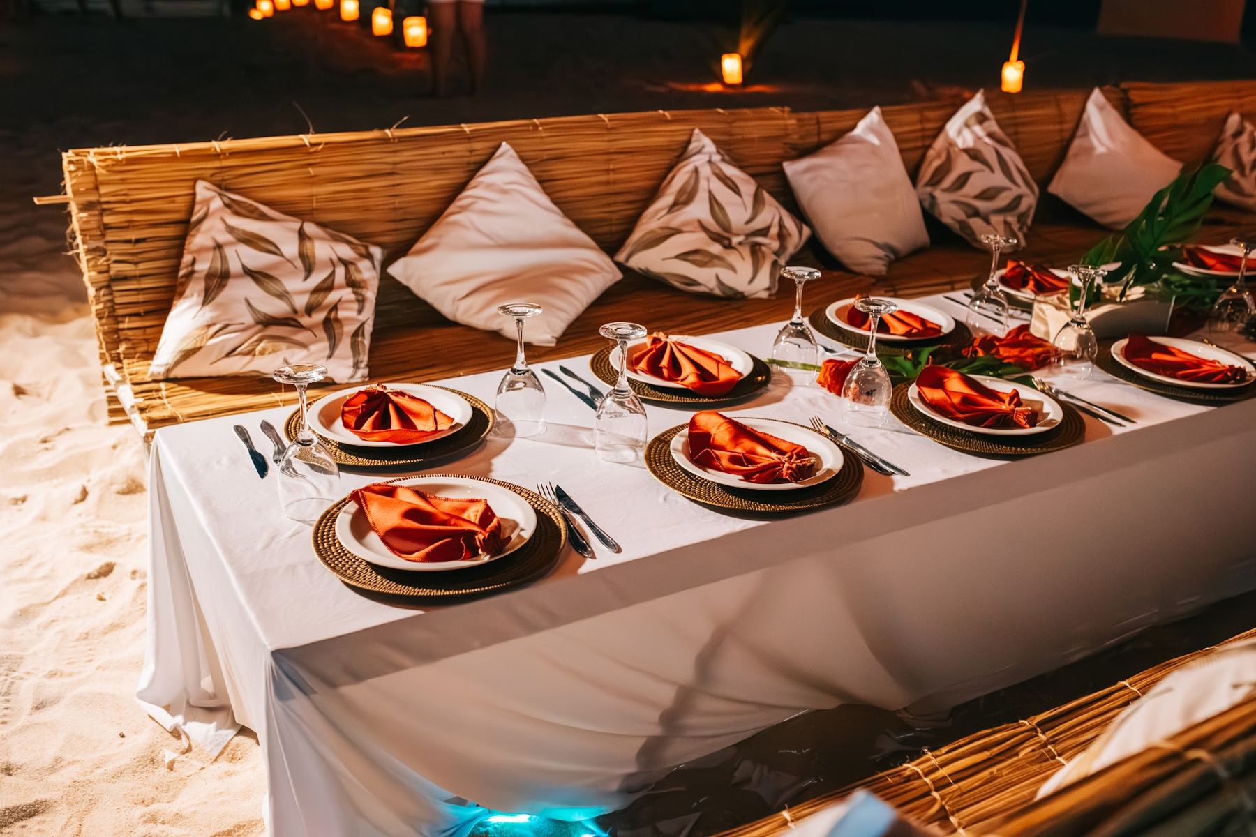 Mesa posta na areia com pratos, almofadas e decoração